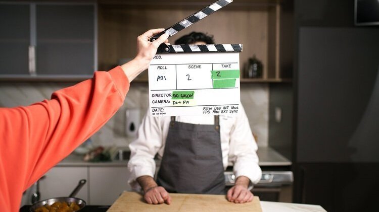 Clap de cinéma devant un cuisinier en tablier dans une cuisine moderne.